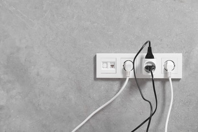 Photo of Many different electrical power plugs in sockets on grey wall, space for text