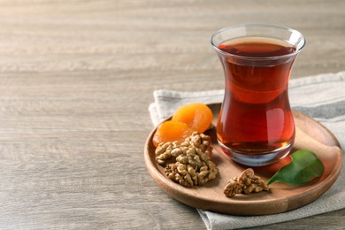 Photo of Board with glass of traditional Turkish tea, walnuts and dried apricots on wooden table. Space for text