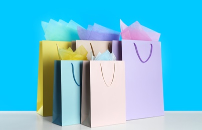 Photo of Colorful gift bags with paper on white table against light blue background
