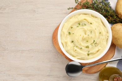 Photo of Bowl of tasty mashed potato with rosemary and olive oil on beige wooden table, flat lay. Space for text