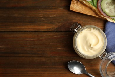 Jar of delicious mayonnaise near fresh sandwich on wooden table, flat lay. Space for text