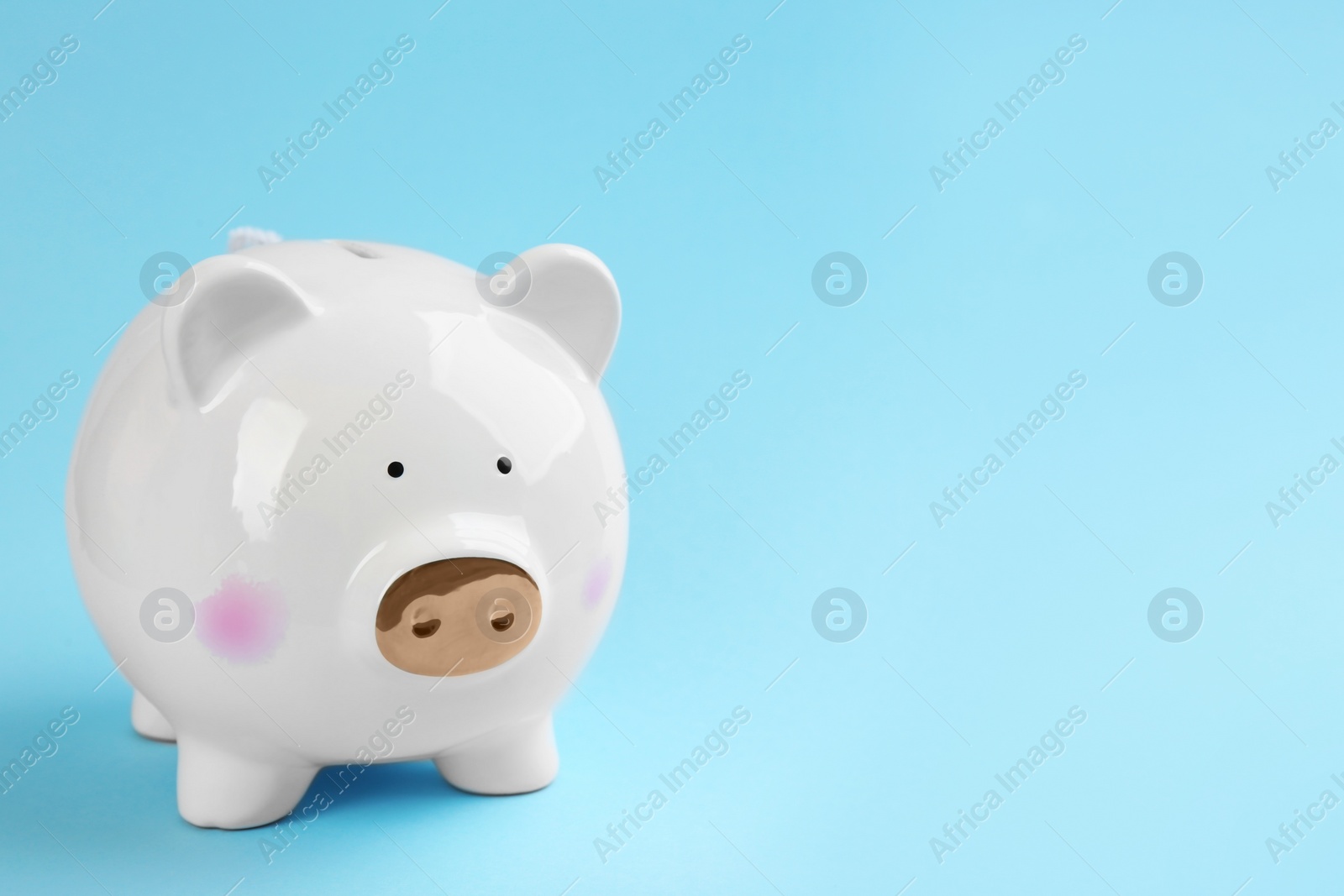 Photo of White piggy bank on light blue background. Space for text