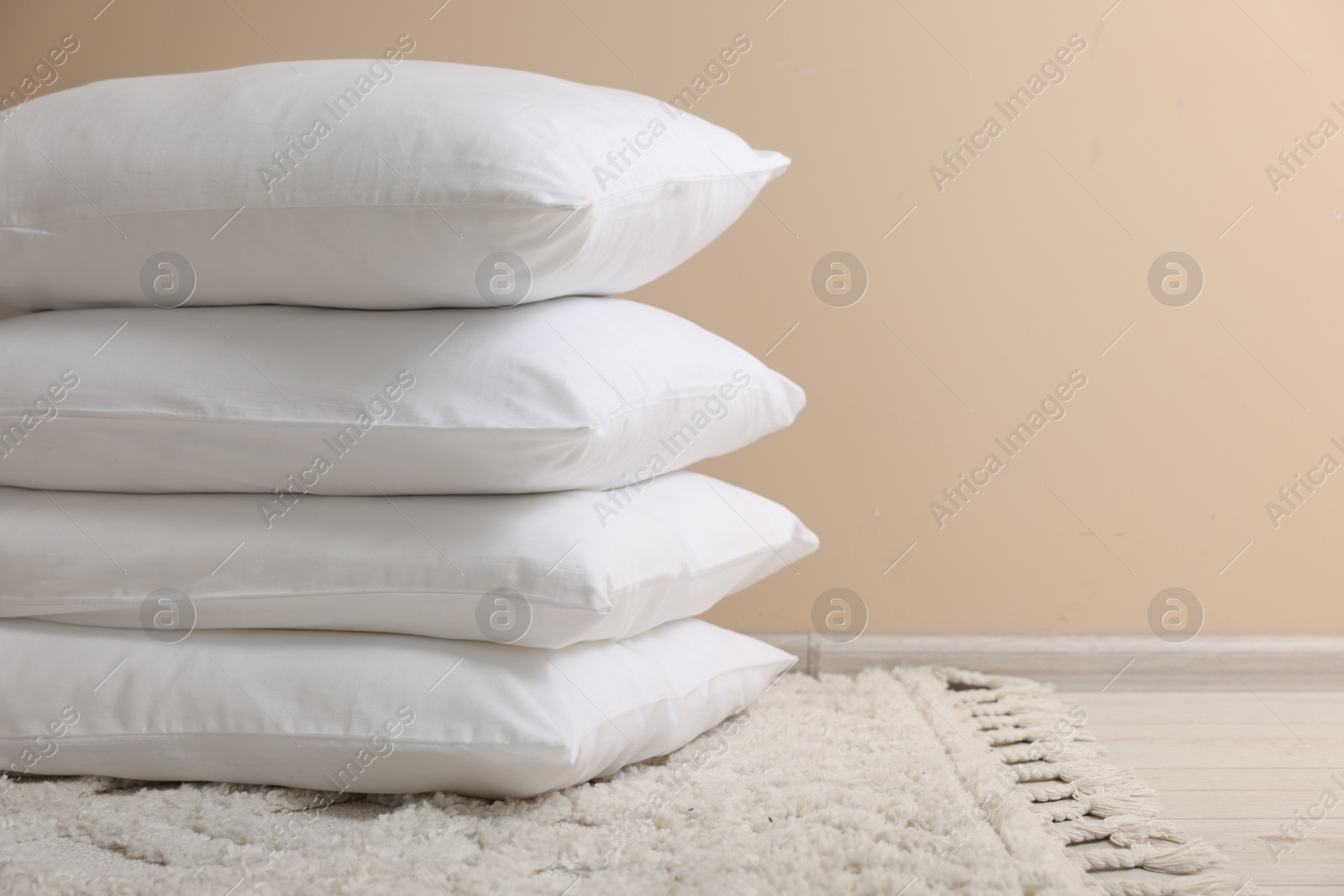 Photo of Stack of soft white pillows near beige wall indoors. Space for text