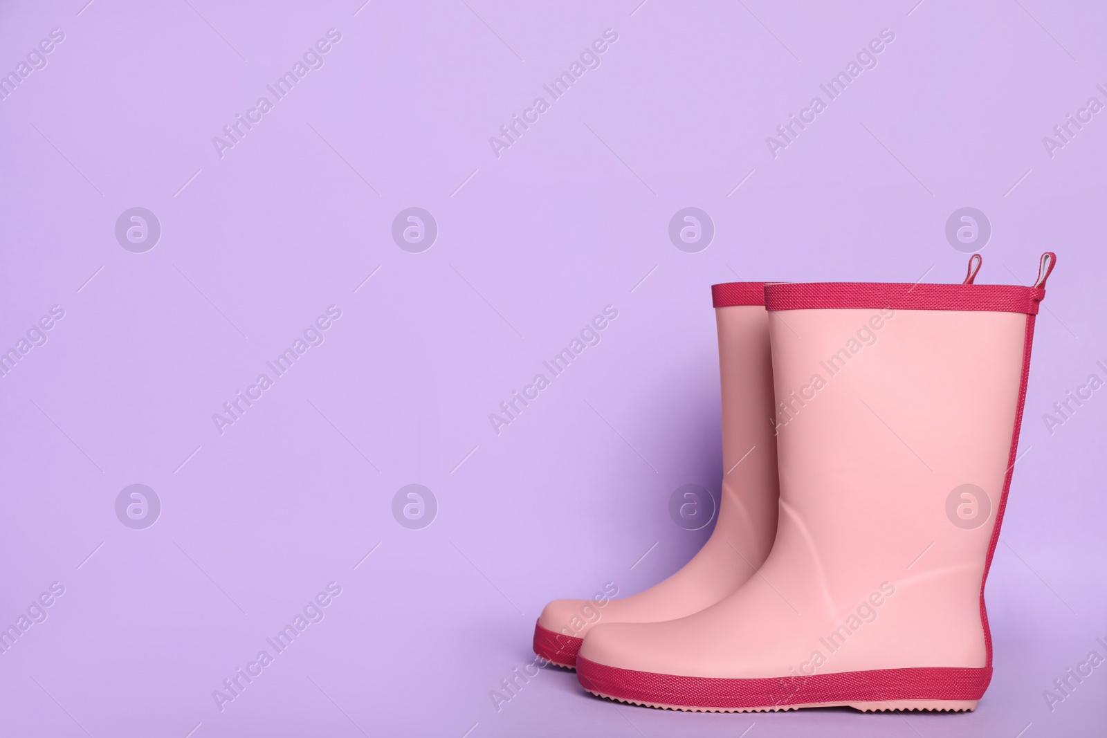 Photo of Pair of pink rubber boots on violet background. Space for text