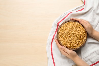 Photo of Woman holding bowl of wheat grains at white wooden table, top view. Space for text