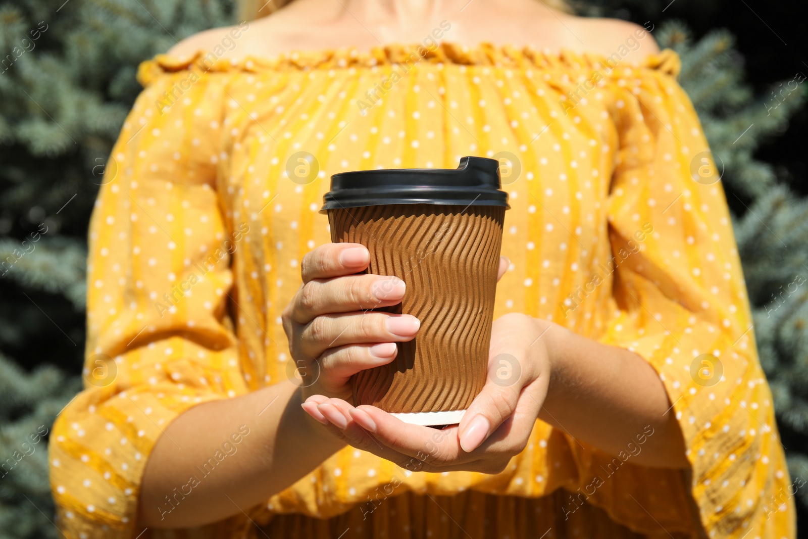 Photo of Woman holding takeaway cardboard coffee cup with plastic lid outdoors, closeup