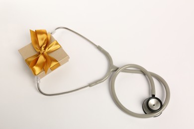 Photo of Stethoscope and gift box on white background, flat lay. Happy Doctor's Day