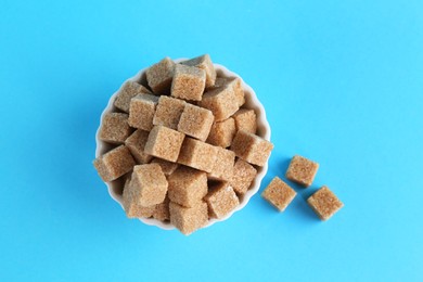 Photo of Brown sugar cubes in bowl on light blue background, top view