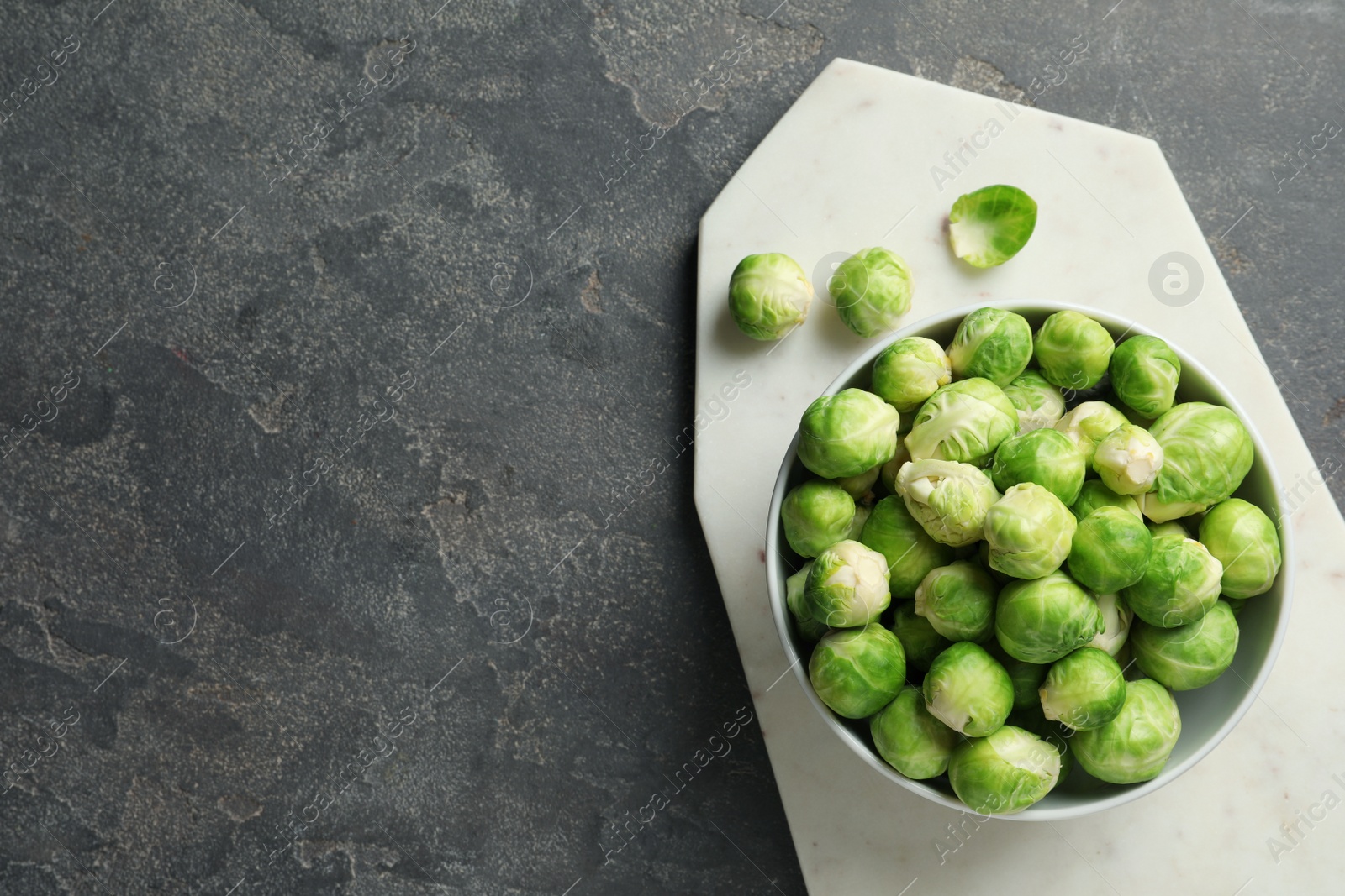 Photo of Board with bowl of Brussels sprouts on grey background, top view. Space for text