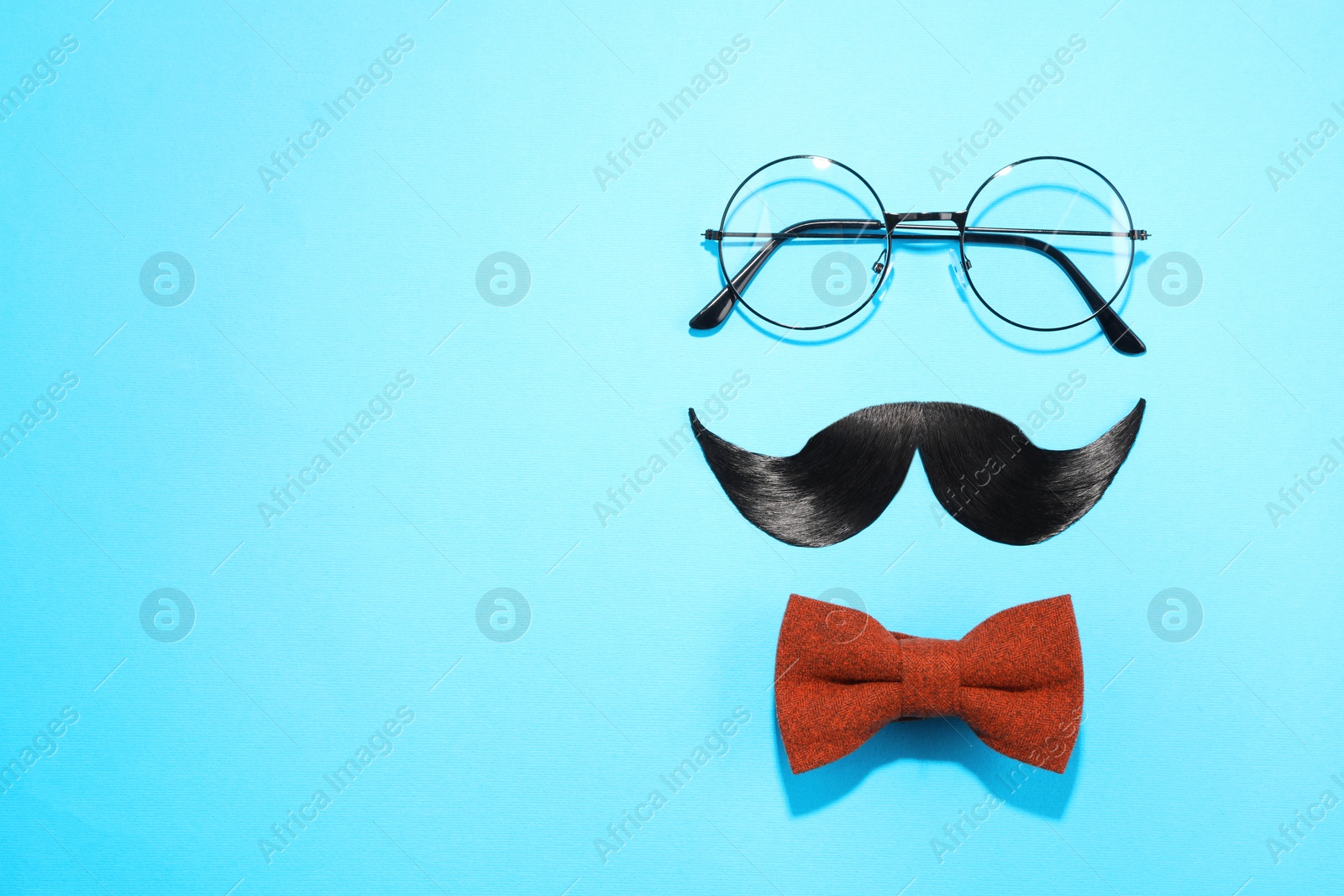 Photo of Artificial moustache, bowtie and glasses on light blue background, flat lay. Space for text