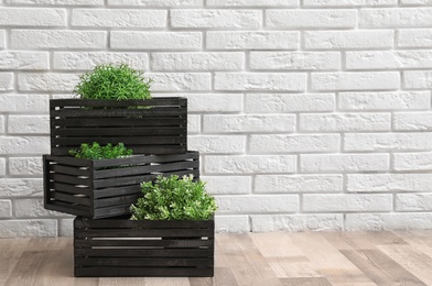 Creative composition of decorative wooden crates with houseplants near brick wall, space for text. Interior decor