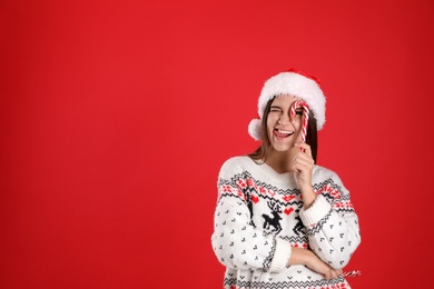 Photo of Pretty woman in Santa hat and Christmas sweater holding candy canes on red background, space for text