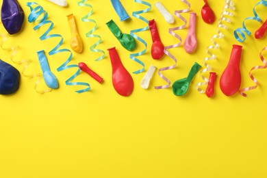 Colorful serpentine streamers and balloons on yellow background, flat lay. Space for text