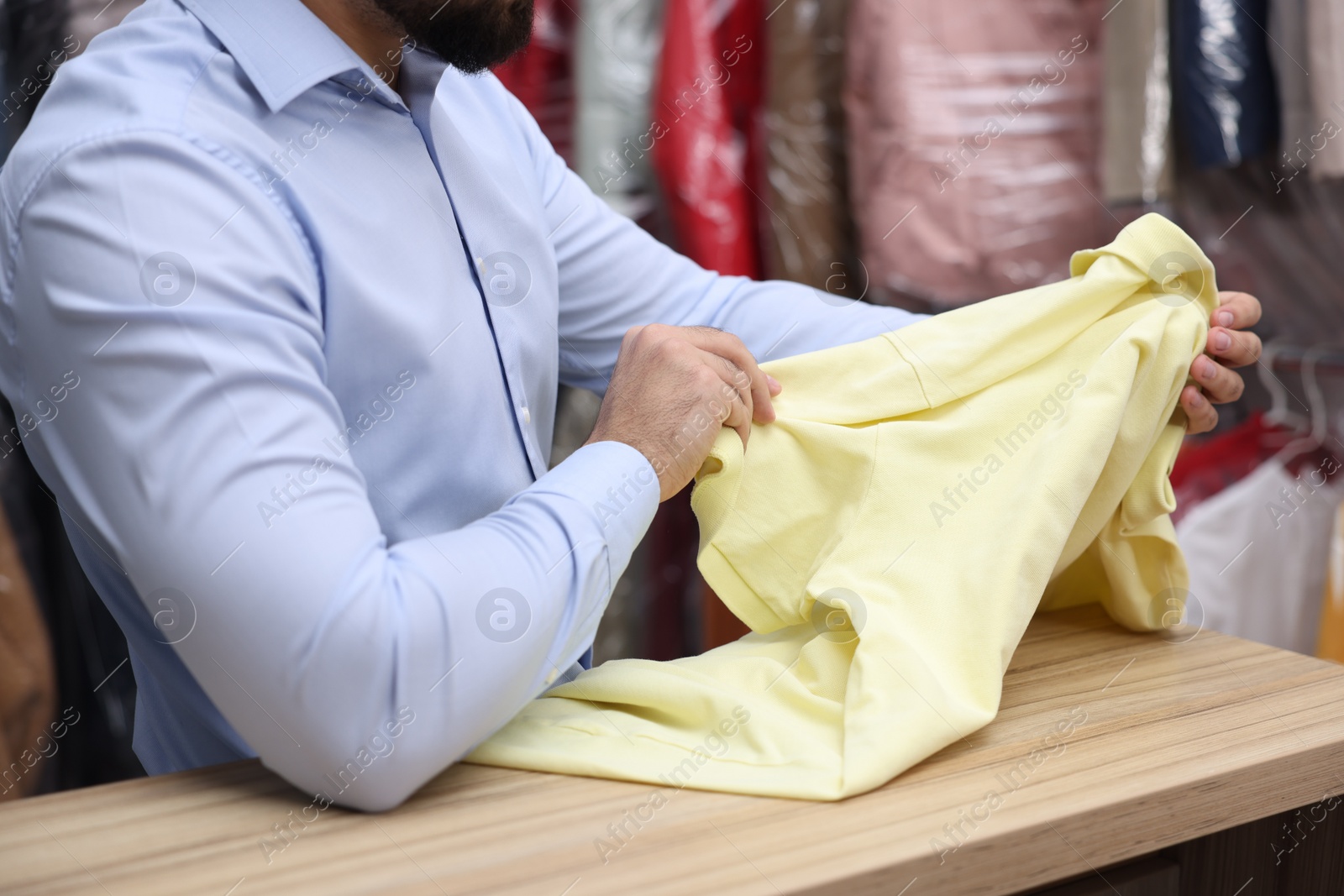 Photo of Dry-cleaning service. Worker holding t-shirt at counter indoors, closeup