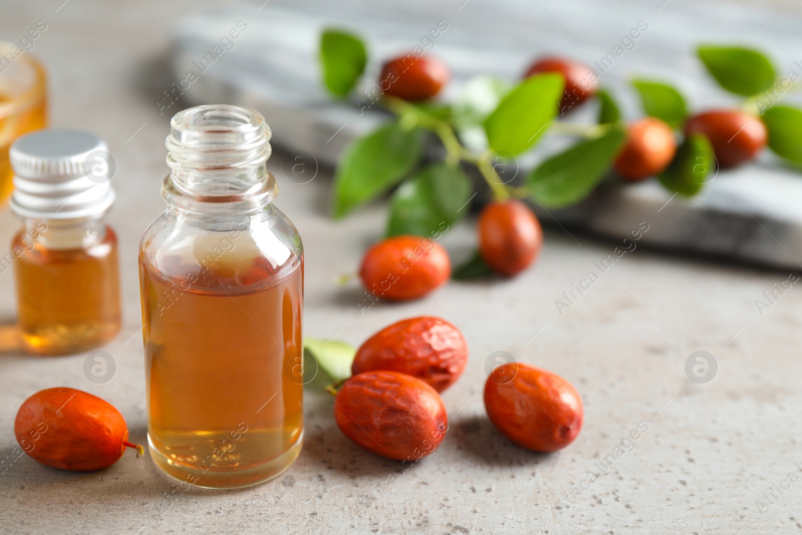 Photo of Glass bottle with jojoba oil and seeds on grey stone table. Space for text