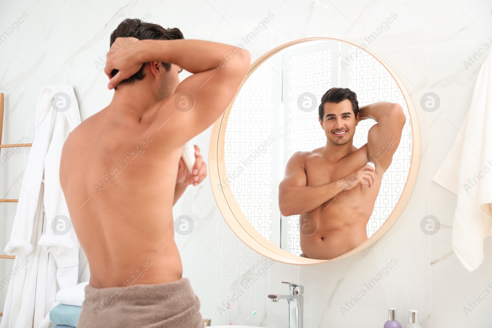 Photo of Handsome young man applying deodorant in bathroom