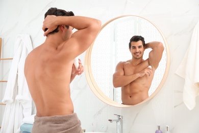 Handsome young man applying deodorant in bathroom