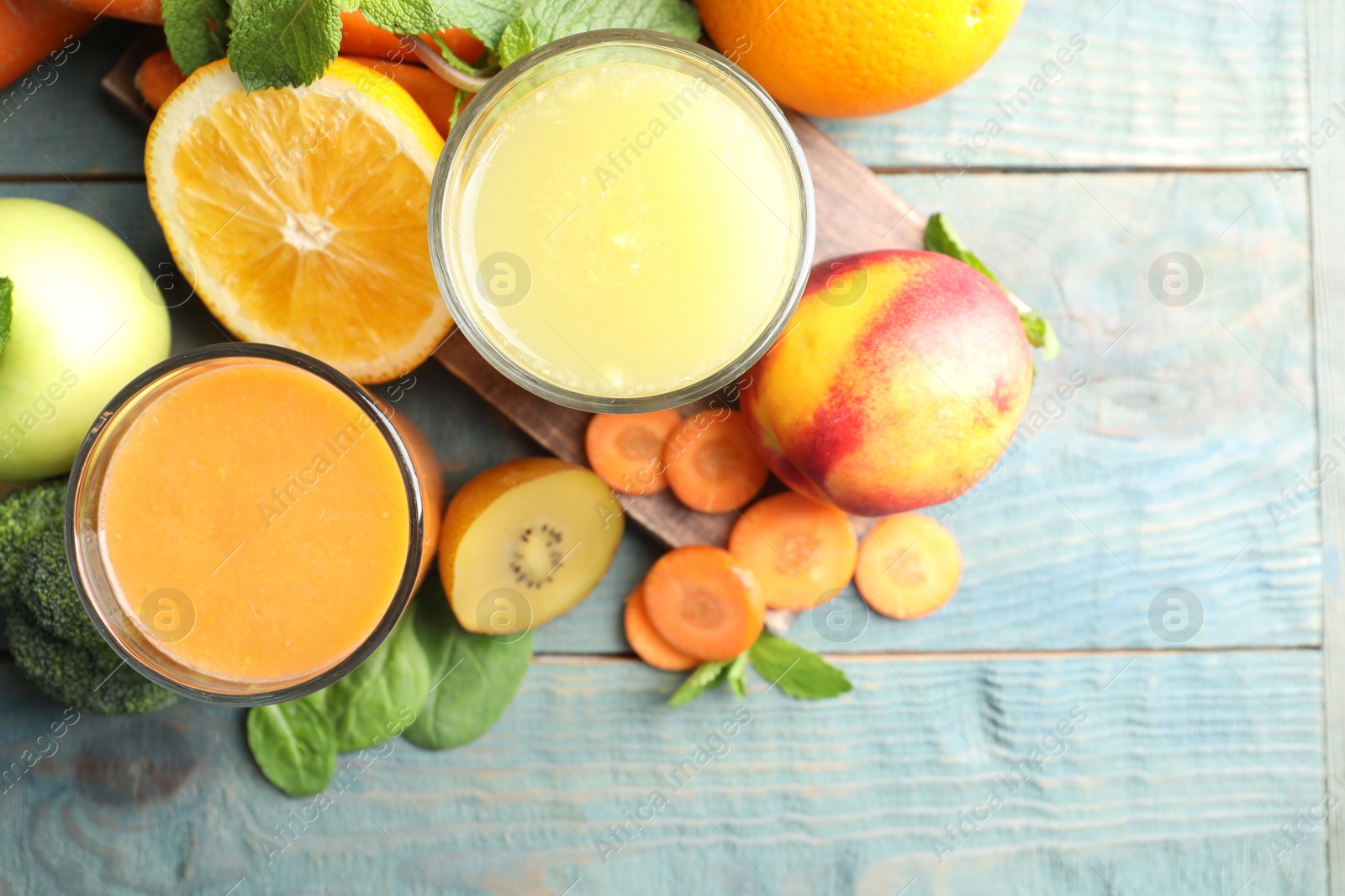 Photo of Glasses of delicious juices and fresh ingredients on blue wooden table, flat lay