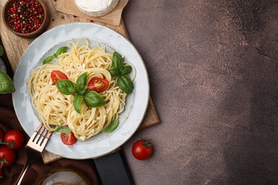 Photo of Delicious pasta with brie cheese, tomatoes and basil leaves served on brown table, flat lay. Space for text