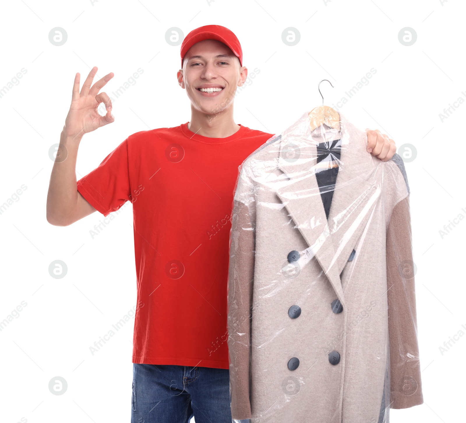 Photo of Dry-cleaning delivery. Happy courier holding coat in plastic bag and showing OK gesture on white background