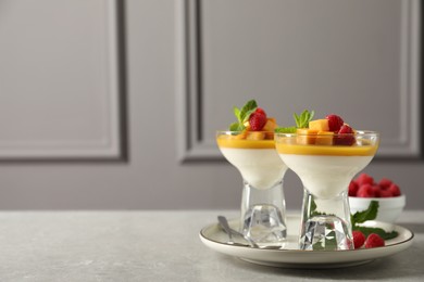 Photo of Delicious panna cotta with mango and raspberries on grey table. Space for text