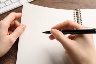 Photo of Woman writing in notebook at wooden table, closeup