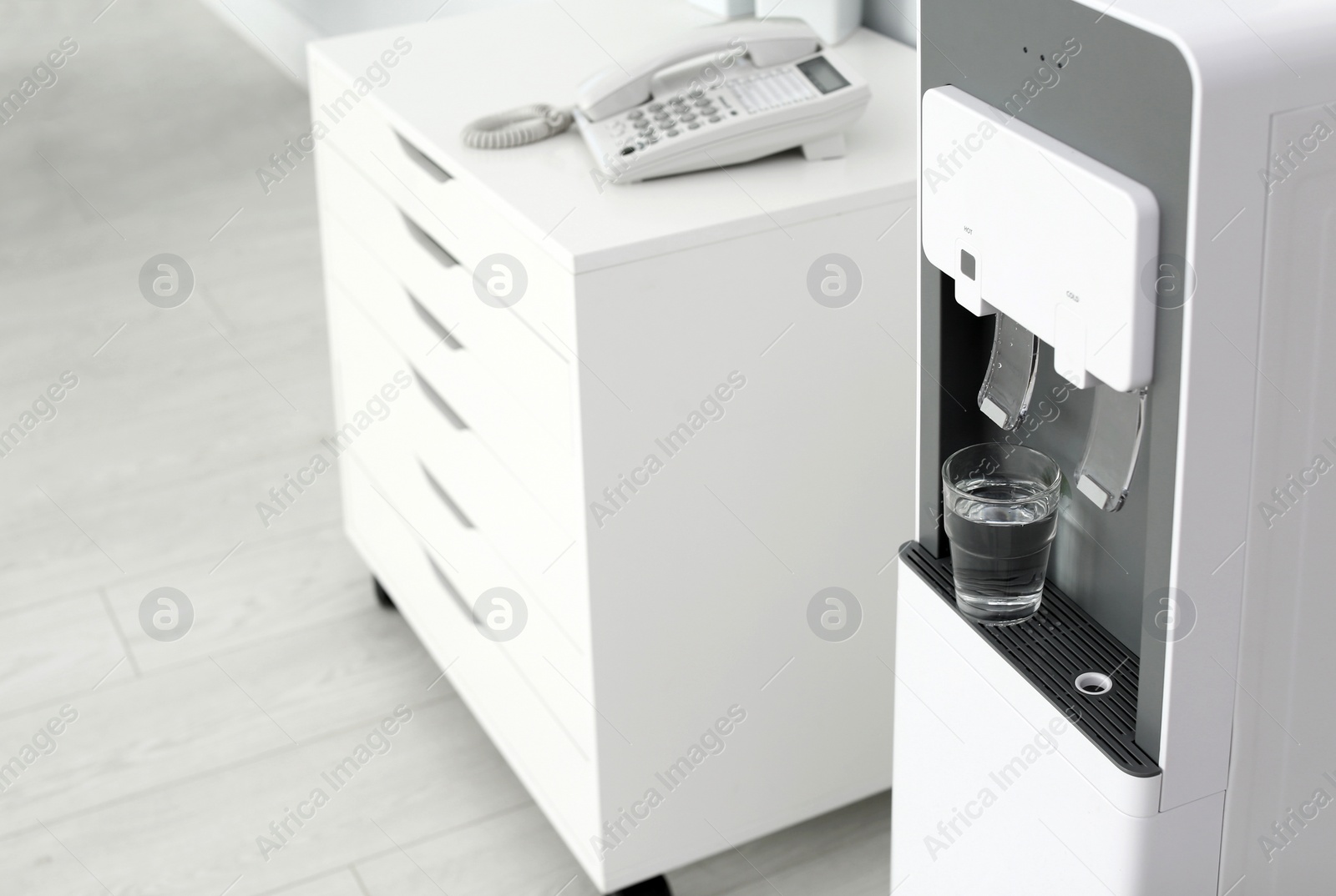 Photo of Modern water cooler with glass in office. Space for text