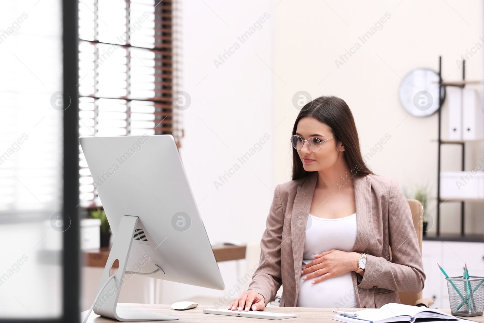 Photo of Young pregnant woman working with computer at table in office