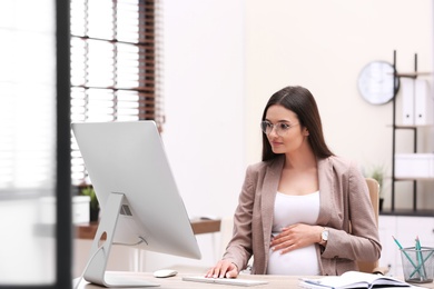 Young pregnant woman working with computer at table in office