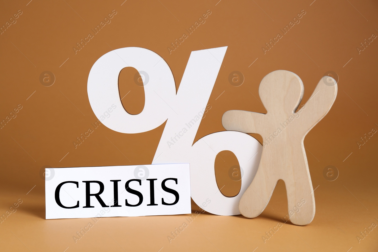 Photo of Wooden human figure near percent sign and word Crisis on brown background