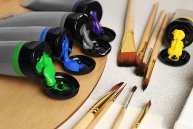 Tubes of colorful paints and brushes on textured table, closeup