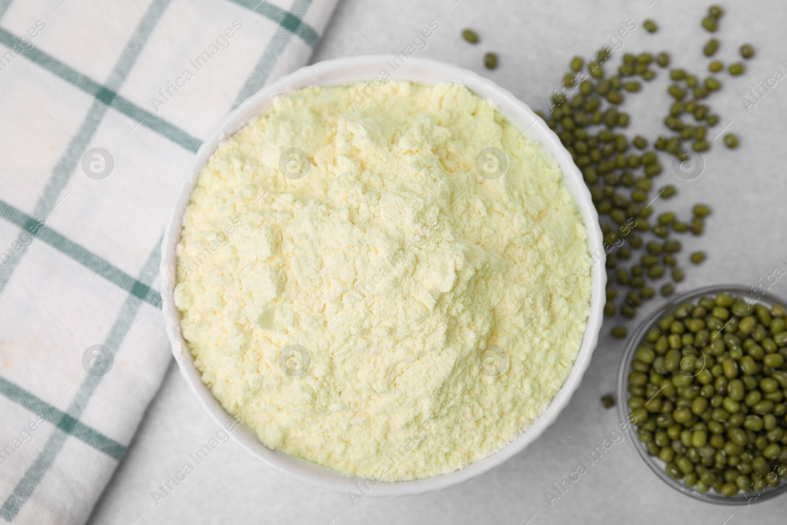 Photo of Mung bean flour in bowl and seeds on white table, flat lay