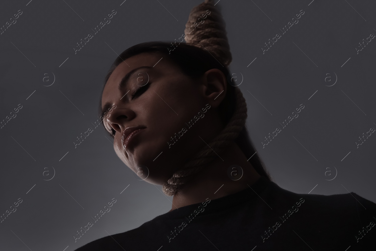 Photo of Depressed woman with rope noose on neck against grey background, low angle view