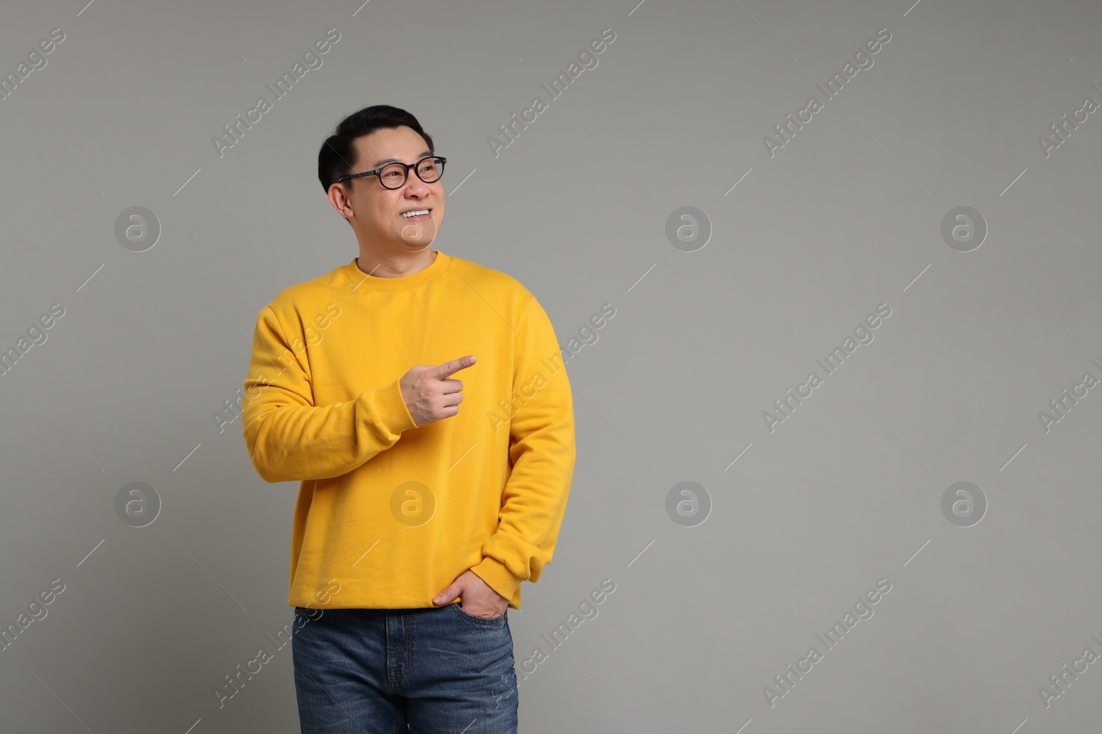 Photo of Portrait of happy man pointing at something on grey background. Space for text