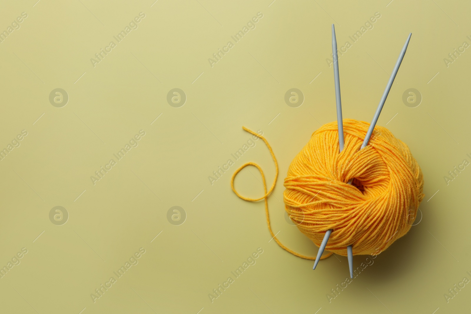 Photo of Soft woolen yarn and knitting needles on yellow background, top view. Space for text