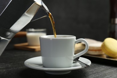 Photo of Pouring coffee from moka pot into cup at dark textured table, closeup