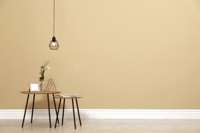 Photo of Small tables with decor near beige wall in room, space for text. Interior design