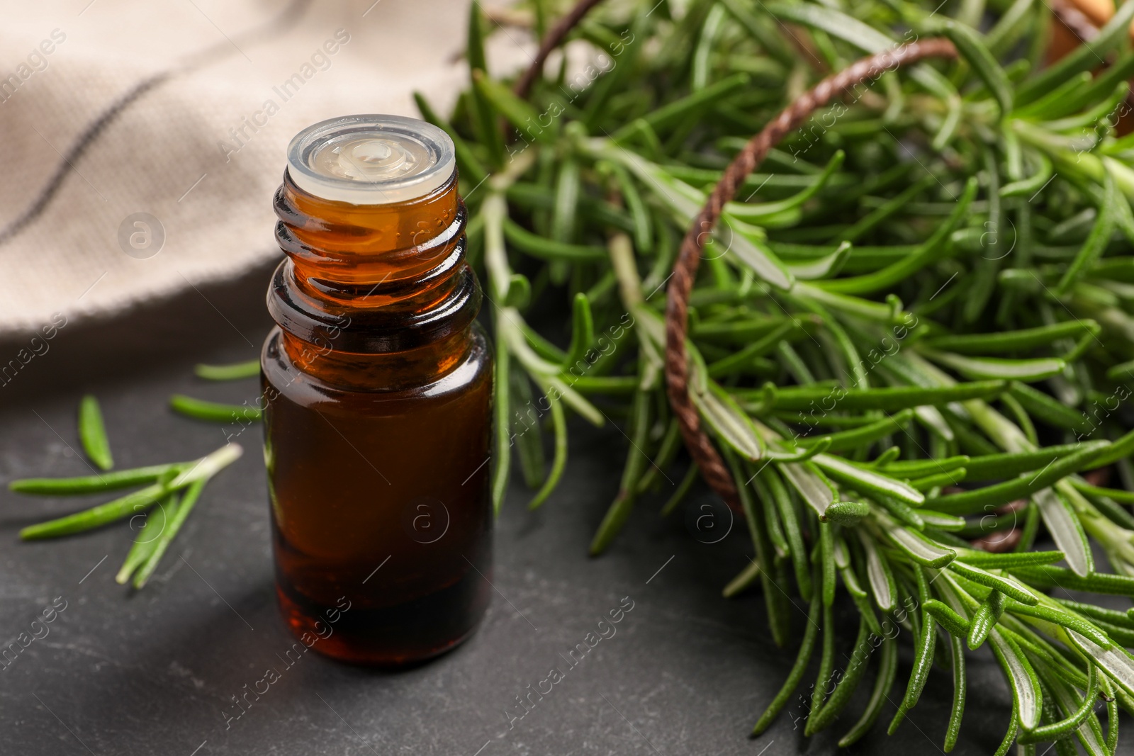 Photo of Bottle of essential oil and fresh rosemary on black table, closeup