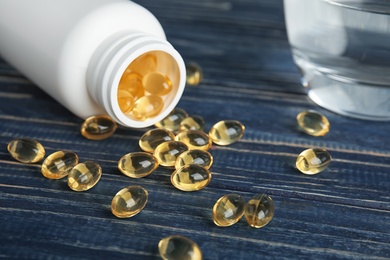 Cod liver oil pills and glass of water on table, closeup