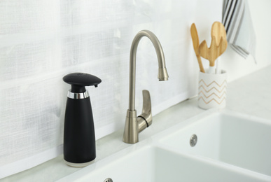 Photo of Modern automatic soap dispenser near sink in kitchen