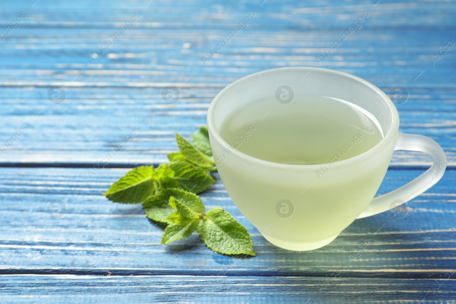 Photo of Cup with hot aromatic mint tea and fresh leaves on wooden table