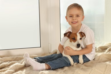 Photo of Little boy with his cute dog on windowsill at home, space for text. Adorable pet