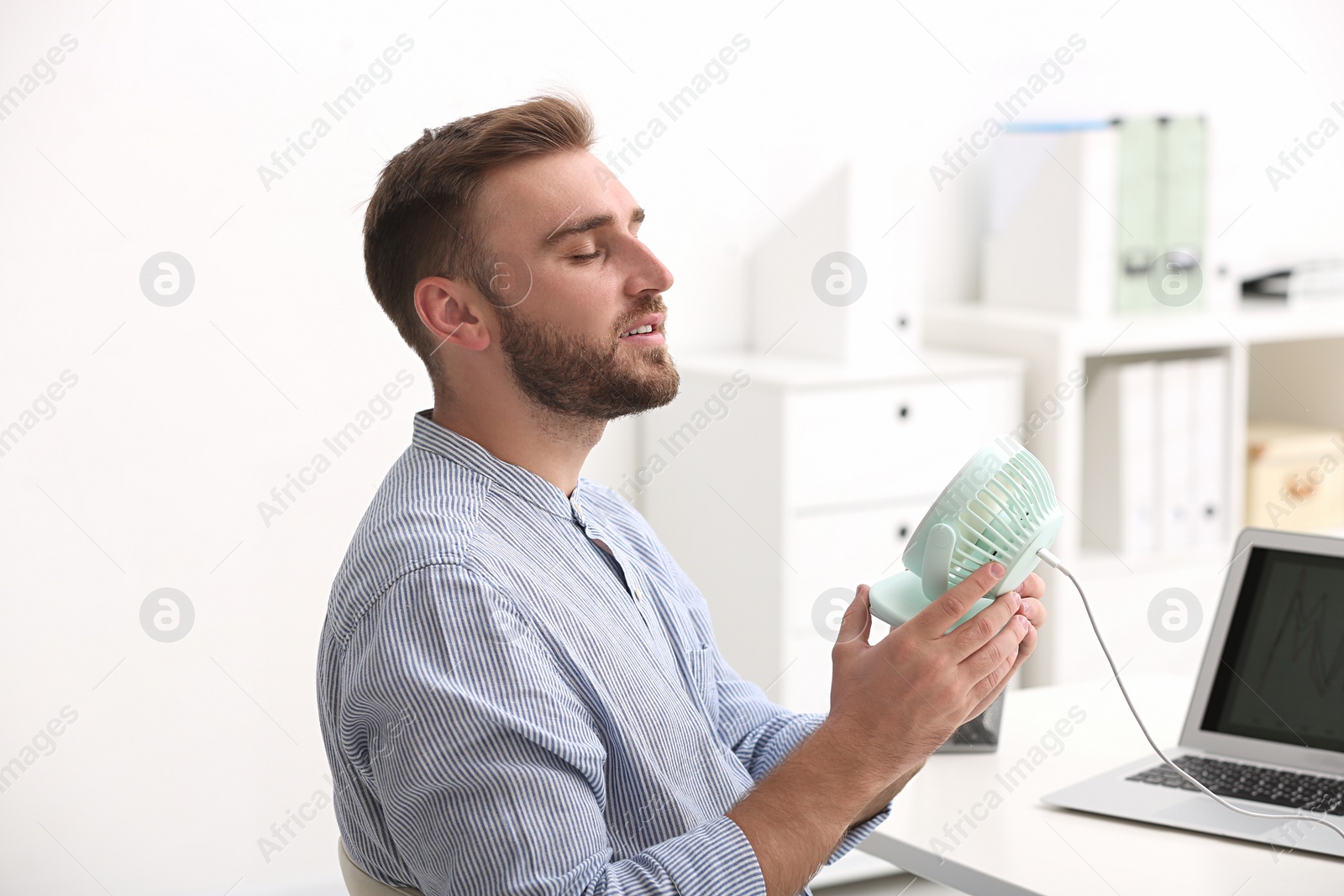 Photo of Man enjoying air flow from fan at workplace