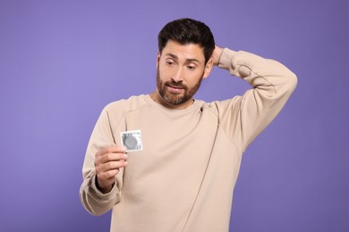 Photo of Confused man holding condom on purple background. Safe sex