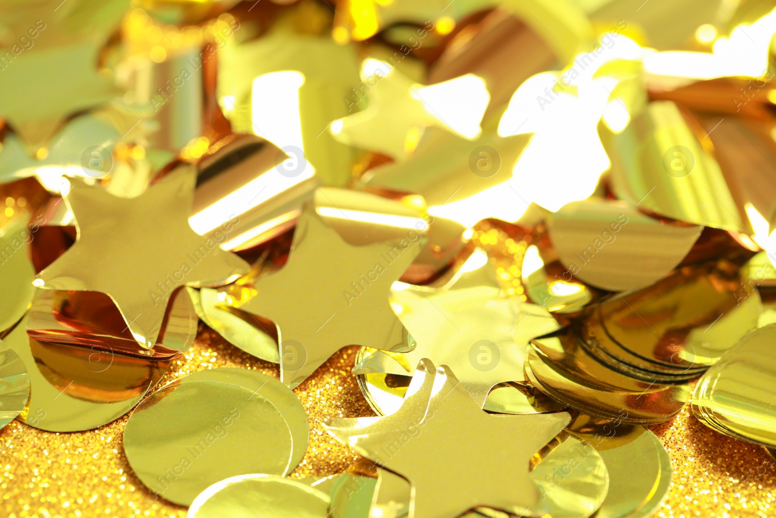 Photo of Beautiful golden confetti on shiny glitter, closeup