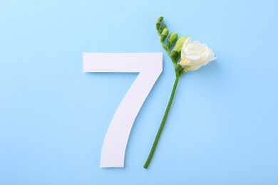 Paper number 7 and beautiful flower on light blue background, top view