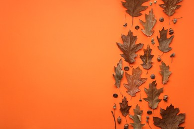 Dry autumn leaves and acorns on orange background, flat lay. Space for text