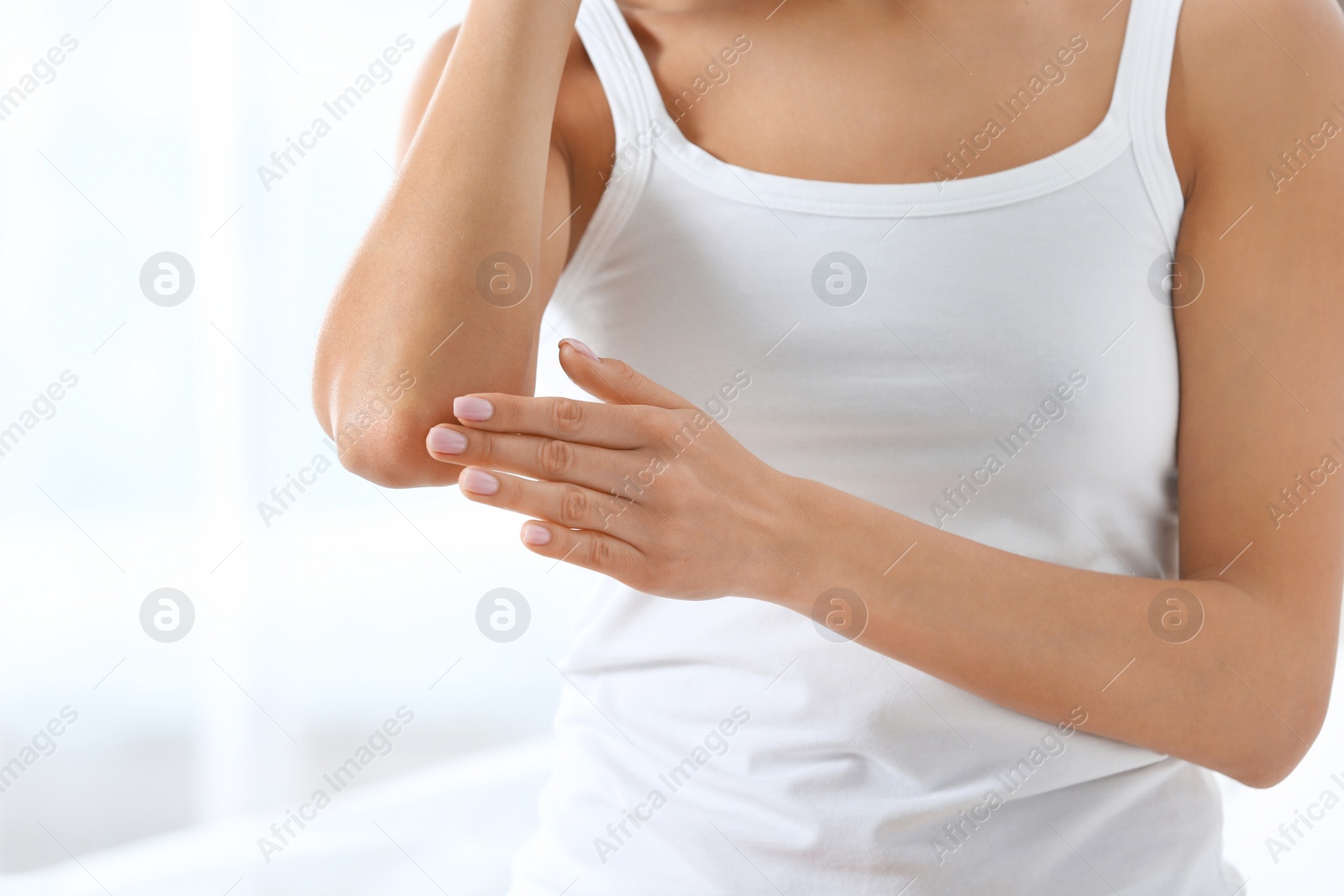 Photo of Young woman applying cream on light background, closeup. Beauty and body care