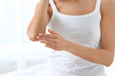 Young woman applying cream on light background, closeup. Beauty and body care