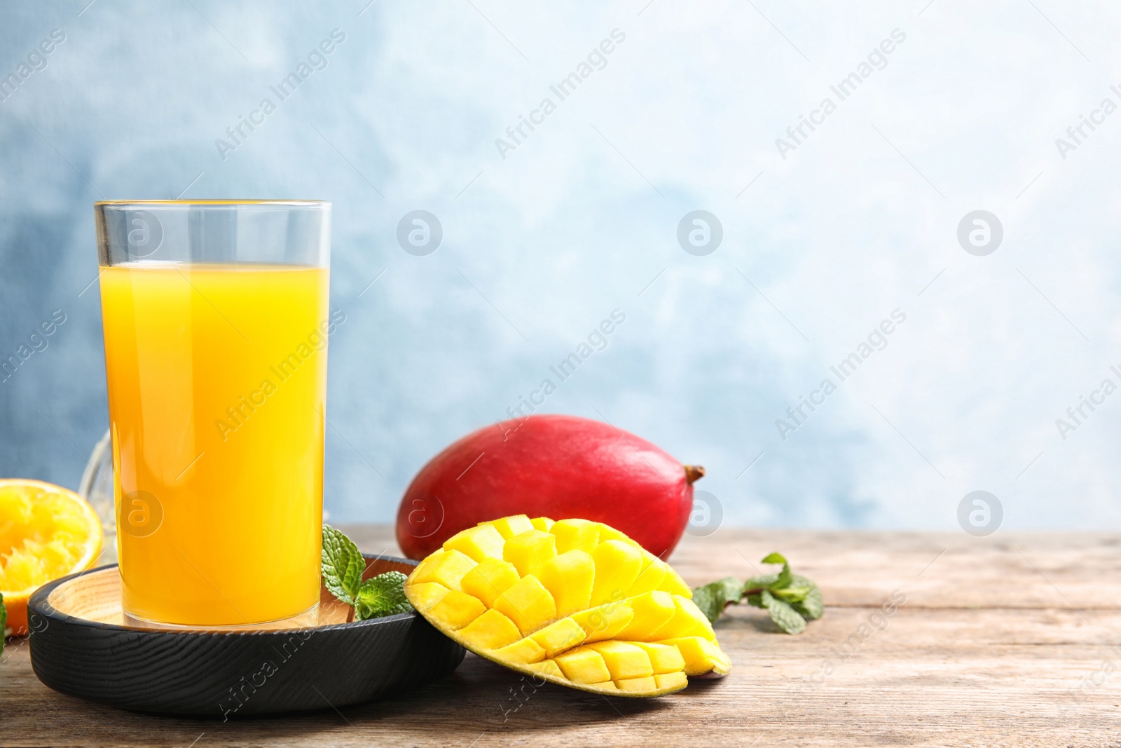 Photo of Glass of fresh mango drink and tropical fruits on table against color background. Space for text